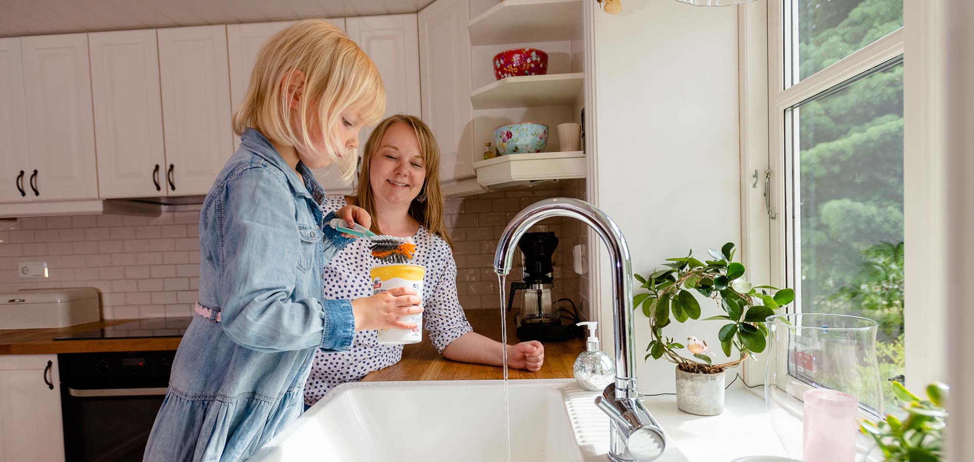 Liten jente og mamma vasker plast med oppvaskbørste.